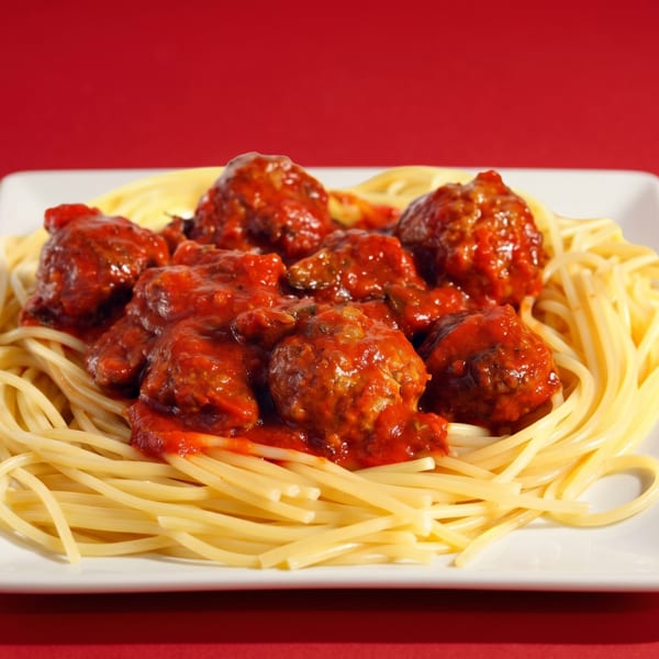 Spaghetti and meatballs with red sauce on a white rectangular plate against a red background.