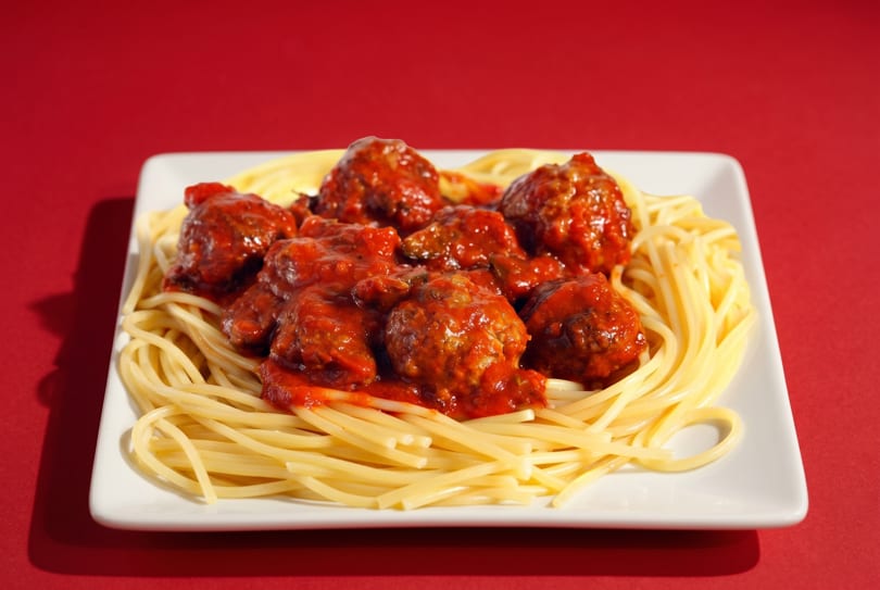 Spaghetti and meatballs with red sauce on a white rectangular plate against a red background.