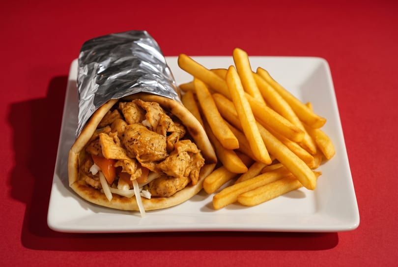 Chicken gyro wrapped in foil with a side of golden french fries on a white plate.